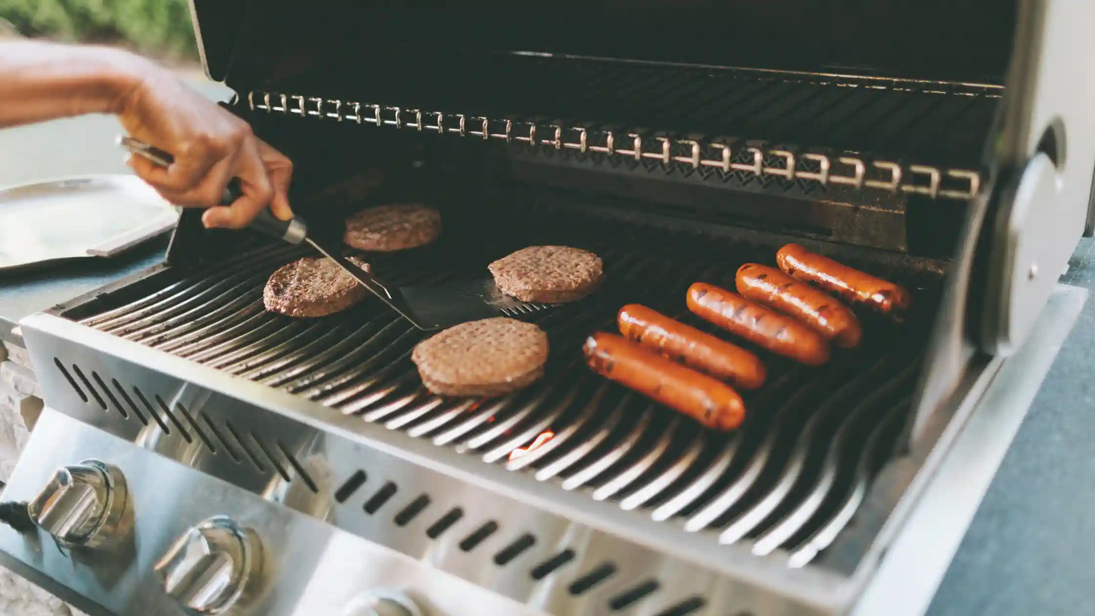 Sausage links and hot dogs cooking on an outdoor barbecue, highlighting safe grilling practices and fire prevention during summer cookouts.