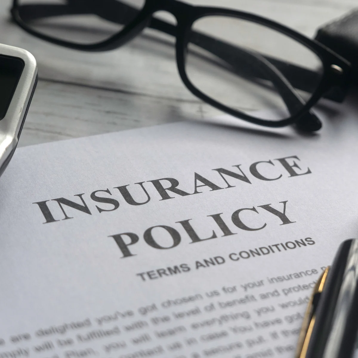 Insurance policy paperwork with glasses and a pen, representing considerations for homeowners deciding whether to file a claim or pay for minor repairs.
