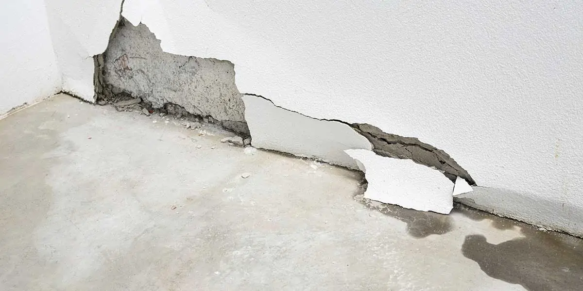 Cracked and peeling basement wall showing concrete damage from water seepage along the interior floor line and foundation wall.